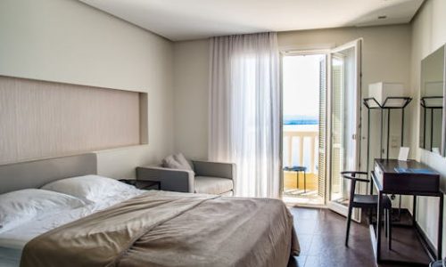 Spacious, elegantly furnished hotel room featuring a balcony with a sea view and modern amenities.